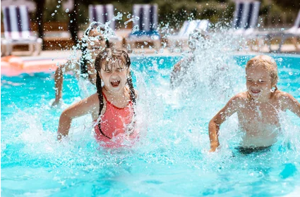 Two children splash and play in a sunny outdoor swimming pool.